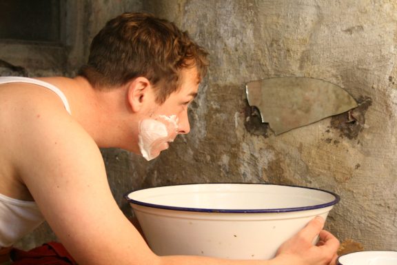 Mann mit Rasierschaum im Gesicht, schaut in eine Waschschüssel.