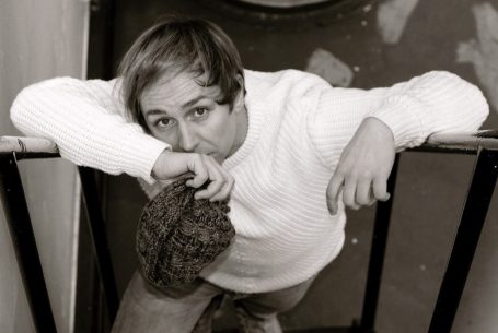 Junger Mann lehnt sich an eine Treppe und schaut direkt in die Kamera.